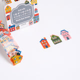 A roll of Japanese washi paper tape house stickers, each featuring a different little house or mansion. Pictured with its packaging and available at NiMi Projects UK.