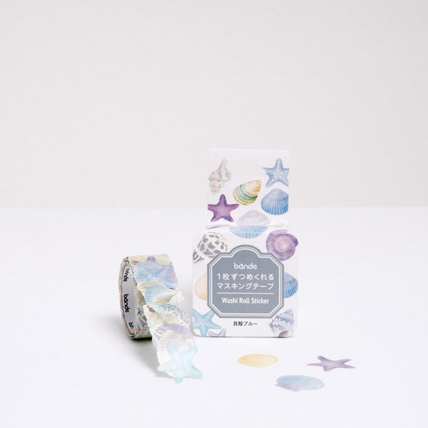A roll of Japanese washi paper tape blue tone seashell stickers, each featuring a different sea shell. Pictured with its packaging and available at NiMi Projects UK.