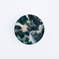 A recycled marine plastic coaster made by Buoy in Japan and available at NiMi Projects. The coaster's mottled black colour includes flecks of white and deep green, and is produced by the original colours of plastics waste collected from the coasts of Japan.