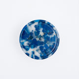 A recycled marine plastic coaster made by Buoy in Japan and available at NiMi Projects. The coaster's mottled blue colour includes flecks of white, and is produced by the original colours of plastics waste collected from the coasts of Japan.