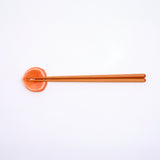 An ariel view of the Ceramic Japan Hanaemu bright orange, porcelain rose petal-shaped chopstick rest, paired with wooden chopsticks. Available as a set at NiMi Projects UK. 