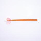 An ariel view of the Ceramic Japan Hanaemu blush pink, porcelain carnation petal-shaped chopstick rest, paired with wooden chopsticks. Available as a set at NiMi Projects UK. 