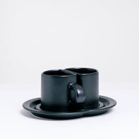 Two black semi-circle cups, made by Ceramic Japan, that sit together with their flat sides meeting on a shared double saucer, on show at NiMi Projects UK.