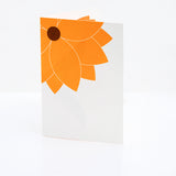 A front shot of a Chisato Tamabayashi orange flower 3D popup greeting card, showing a partial graphic of bright orange flower on the top left corner on a white background. Available at NiMi Projects UK.