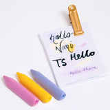 Three NiMi Projects' triangular Sakura Coupy dry highlighter crayons in pink, yellow and lilac, with a notepad and golden clip.