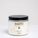 A short, cylindrical glass jar of bath salts with a flat, black, metal screwtop lid. The jar has EARTH written on it, and the Japanese kanji for earth, with "homework" written below. Available at NiMi Projects UK.