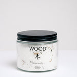 A short, cylindrical glass jar of bath salts with a flat, black, metal screwtop lid. The jar has WOOD written on it, and the Japanese kanji for wood, with "homework" written below. Available at NiMi Projects UK.