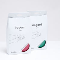 Two Japanese Irogami stainless steel graters — one pink and one green — in their paper packaging illustrated with a line drawing of how to use the grater. Made in Japan and available at NiMi Projects.