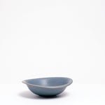A side view of a Mino-yaki Japanese porcelain dessert bowl, featuring an asymmetric curved rim and soft blue, flecked glaze. On show at NiMi Projects UK.