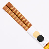 A detail shot of a pair of Japanese, wooden chopsticks featuring thin stripes of bright yellow.