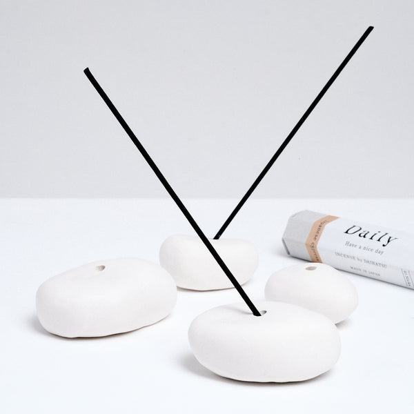 A group of four white, ceramic pebble-shaped stick incense holders made by ceramicist Maki Baxter and available at NiMi Projects UK. Two of the pebbles are holding Daily Japanese incense by Trunk Design. 