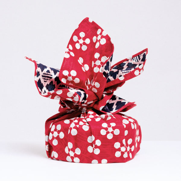 A gift wrapped in a Musubi Japanese furoshiki wrapping cloth, featuring a pattern of apricot flowers on a red background on one side and a geometric pattern of bamboo and pine bark in white on navy blue on the other side. Made in Japan and available at NiMi Projects UK