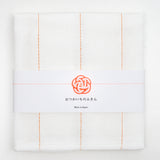 Ariel view of a white, folded Japanese fukin kitchen cloth, detailed with orange, vertical stitched lines and wrapped in a white slip with a white and orange mizuhiki paper cord knot in a traditional design of a plum blossom. Available at NiMi Objects.