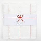 Top view of a white, folded Japanese fukin kitchen cloth, detailed with red vertical stitched lines and wrapped in a white slip with a red and white mizuhiki paper cord knot in a traditional design of a flower in a bow. Available at NiMi Objects.