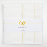 Top view of a white, folded Japanese fukin kitchen cloth, detailed with yellow vertical stitched lines and wrapped in a white slip with a yellow and white mizuhiki paper cord knot in a traditional design of a butterfly. Available at NiMi Objects.