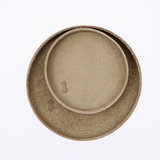 Ariel view of a small, round, green-beige, up-cycled skived split leather tray on top of a larger version. The trays have been molded into shape by Japanese leather artisans Rhythmos and is available at NiMi Projects UK.
