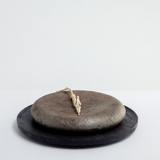 A round, deep blond wild cherry wood pedestal plate finished with washi paper and urushi lacquer with a dusting of tin powder laid on top of a circular flat wild cherry wood plate, finished with a darker lacquer and textured with layers of washi paper. Both are made of thinned wood collected in Yakushima by Japanese artisan Solmu Puut and on show at NiMi Projects UK.