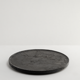 Side view of a large round wild cherry wood plate, textured with layers of washi paper and deep brown lacquer. Made in Japan from wood sourced from thinning projects in Yakushima and hand crafted by wood artisans Solmu Puut. On display with white dried flowers at NiMi Projects UK.