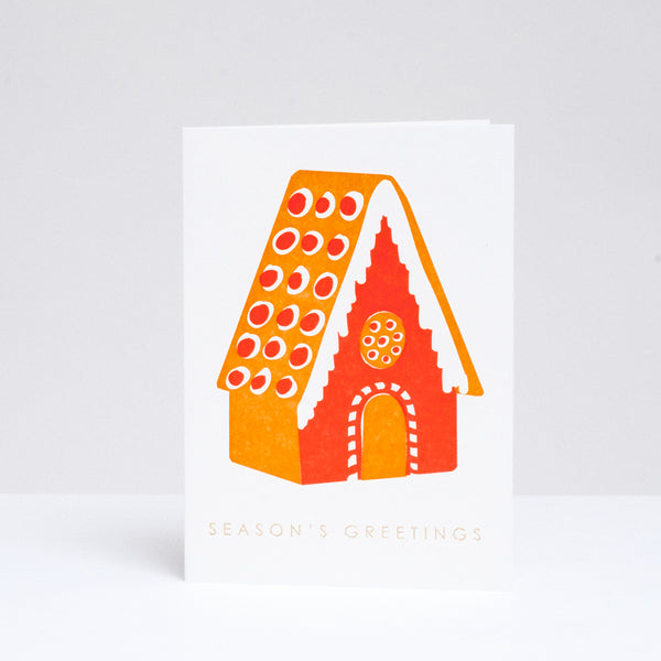 Takako Copeland's Gingerbread House greeting card, featuring a letterpress-printed cinnamon orange and red gingerbread house with and the words “Season’s Greetings” in gold foil. Available at NiMi Projects UK.