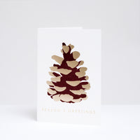 Takako Copeland's Christmas Gold Pine Cone greeting card, featuring a letterpress-printed aubergine-coloured pine cone with gold highlights and the words “Season’s Greetings” in gold foil.
