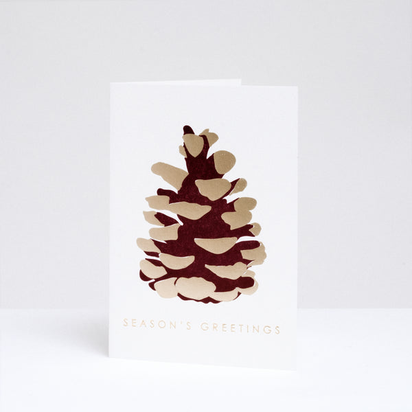 Takako Copeland's Christmas Gold Pine Cone greeting card, featuring a letterpress-printed aubergine-coloured pine cone with gold highlights and the words “Season’s Greetings” in gold foil.