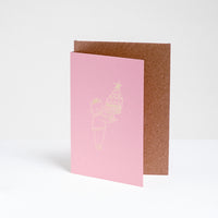 A standing pinke greeting card, designed by Takako Copeland, featuring a gold foil line drawing illustration of a cat in a party crown and sweater holding a large trifle on a platter. Available at NiMi Projects UK. 
