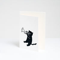 A standing white greeting card featuring a Takako Copeland illustration of a black cat playing a trumpet. Available at NiMi Projects UK.
