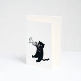A standing white greeting card featuring a Takako Copeland illustration of a black cat playing a trumpet. Available at NiMi Projects UK.
