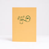  Letterpress printed in green on bright yellow, Takako Copeland's Oxalis Card features an illustration of a bundle of Oxalis growing tall as they are watered by a long-spout watering can.