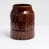 A cylindrical ceramic kitchen tool stand with a geometric pattern of three rows of rectangular indents and glazed in a rich, glossy brown. Made by Angle in Japan and available at NiMi Projects UK.