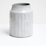 A white glazed, cylindrical ceramic kitchen tool stand with a geometric pattern of three rows of rectangular indents. Available at NiMi Projects UK and made by Angle in Japan.