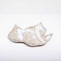 A vintage Japanese ceramic dish in the shape of a maple leaf glazed in natural off-white or light beige and speckled with brown flecks and featuring pattern of dripped milky white glaze.. 
