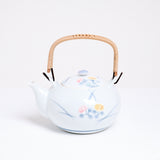 A vintage white porcelain Japanese tea pot featuring a top handle and a design of two hand-painted lilies, one pink and one pale yellow, with blue leaves. Available at NiMi Projects UK.