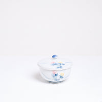A vintage white porcelain Japanese lidded tea cup, showcasing a design of two hand-painted lilies, one pink and one pale yellow, with blue leaves. On show at NiMi Projects UK.