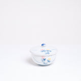A vintage white porcelain Japanese lidded tea cup, showcasing a design of two hand-painted lilies, one pink and one pale yellow, with blue leaves. On show at NiMi Projects UK.