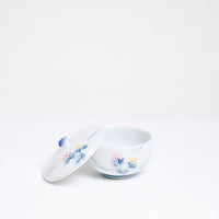 A vintage white porcelain Japanese lidded tea cup, showcasing a design of two hand-painted lilies, one pink and one pale yellow, with blue leaves. Available at NiMi Projects UK.