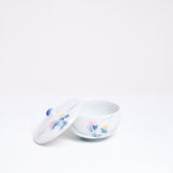 A vintage white porcelain Japanese lidded tea cup, showcasing a design of two hand-painted lilies, one pink and one pale yellow, with blue leaves. Available at NiMi Projects UK.