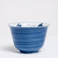 A close up image of a vintage white porcelain Japanese teacup with a hand-painted blue exterior and a blue mountainscape inside. Available at NiMi Projects UK.