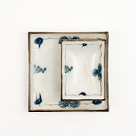 Two Japanese, vintage porcelain dishes — a large square one, with a smaller rectangle one placed on top. Both feature a border design of blue underglaze bunches of grapes and vine leaves and a crackle glaze.