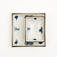 Two Japanese, vintage porcelain dishes — a large square one, with a smaller rectangle one placed on top. Both feature a border design of blue underglaze bunches of grapes and vine leaves and a crackle glaze.