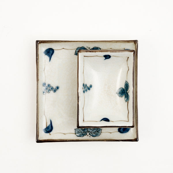 Two Japanese, vintage porcelain dishes — a large square one, with a smaller rectangle one placed on top. Both feature a border design of blue underglaze bunches of grapes and vine leaves and a crackle glaze.