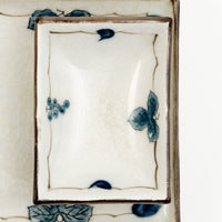 Close up of a small, rectangular, Japanese vintage porcelain dish featuring a border design of blue underglaze bunches of grapes and vine leaves and a crackle glaze