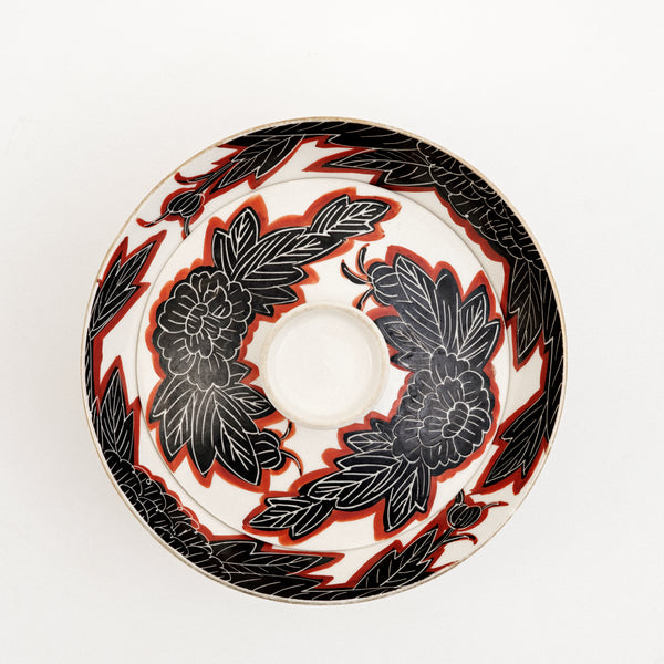 Top view of a white vintage, Japanese porcelain, decorative lidded donburi bowl, showing a bold pattern of peonies in black with white detailing and brick red borders. On show at NiMi Projects UK.