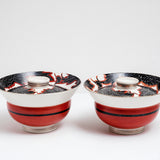 Two vintage, Japanese porcelain, decorative lidded donburi bowls, with a brick red band and black central line on the side and a bold pattern of peonies in black with white detailing and red borders. On show at NiMi Projects UK.