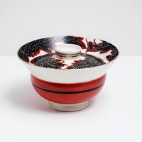 Side view of a white vintage, Japanese porcelain, decorative lidded donburi bowl, showing a bold pattern of peonies in black with white detailing and brick red borders on the lid and a band of brick red on the side. On show at NiMi Projects UK.