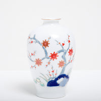 A vintage Japanese porcelain vase in white, with a blue underglaze design of a tree and red painted flowers.