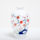 A vintage Japanese porcelain vase in white, with a blue underglaze design of a tree and red painted flowers.