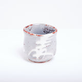 A large vintage Japanese tea cup with off-white, greyish glaze with details of brown speckles. On it's outside is a pattern of brushstrokes resembling the kanji for lucky or wheat.