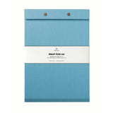A powder blue fabric-covered A4 Postalco Snap Pad, showing the two roundmetal snap clasps at its top and a white label wrapped around its center featuring the Postalco bird logo.