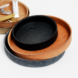 Ariel view of a stack of Rhythmos, up-cycled, skived split leather trays, each round and molded into shape by Rhythmos in Japan. Available at NiMi Projects UK. From top to bottom: A small, deep navy blue tray, a natural beige, and a blue tray.